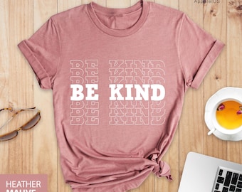 May include: A heather mauve t-shirt with the text "BE KIND" repeated in a stacked pattern. The text is white and outlined in a thin white line.