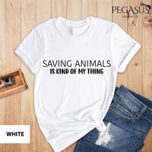 May include: White t-shirt with the text "Saving Animals is Kind of My Thing" printed in black.