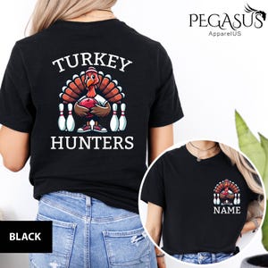 May include: Black t-shirt with a graphic of a turkey holding a bowling ball, surrounded by bowling pins, and the text "TURKEY HUNTERS". A smaller version of the graphic is on the front. The brand name "PEGASUS ApparelUS" is visible.