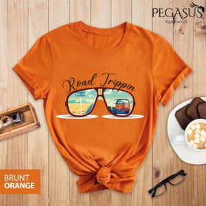 Peut inclure: T-shirt orange avec un graphique de lunettes de soleil refl&eacute;tant une voiture roulant sur la Route 66. Le texte "Road Trippin'" est au-dessus des lunettes de soleil.