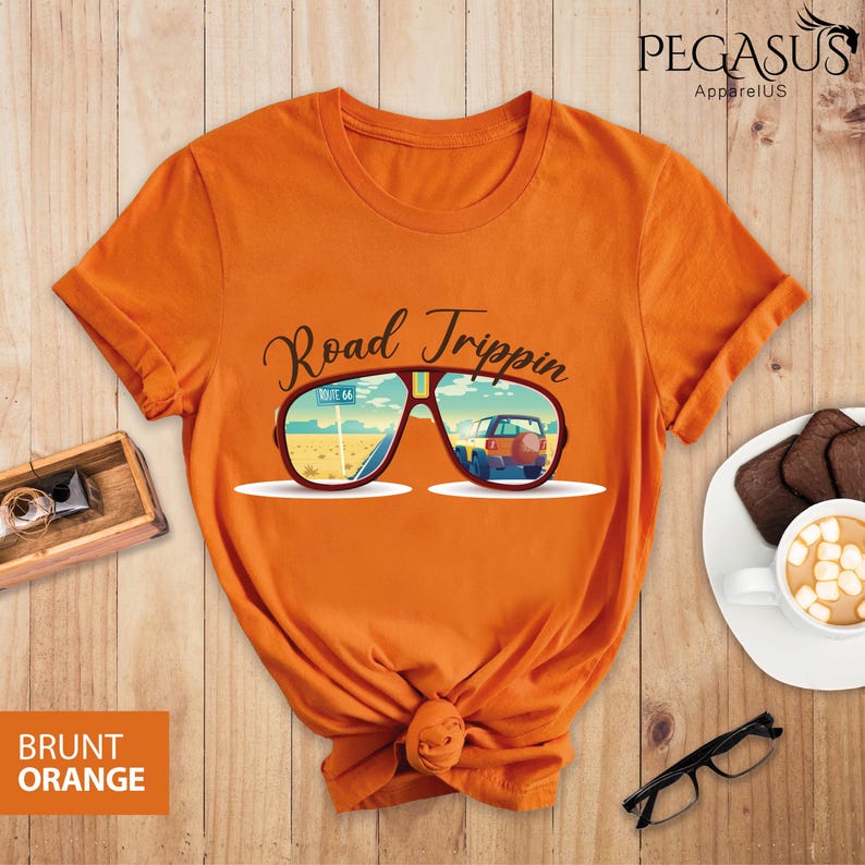 Peut inclure: T-shirt orange avec un graphique de lunettes de soleil refl&eacute;tant une voiture roulant sur la Route 66. Le texte "Road Trippin'" est au-dessus des lunettes de soleil.