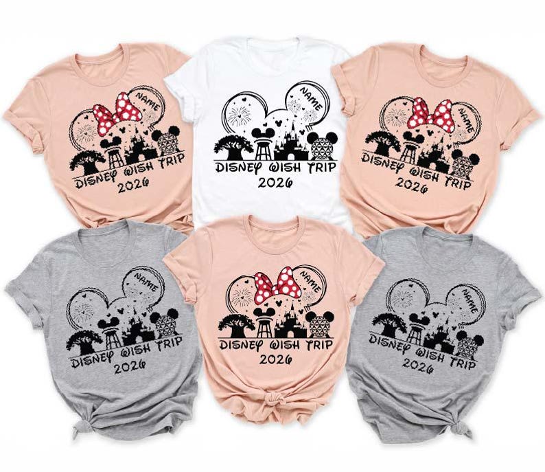 May include: A collection of short-sleeved t-shirts in various colors, including pink, white, and gray. Each shirt features a graphic design with a Minnie Mouse bow, fireworks, and the text "DISNEY WISH TRIP 2026" with a space for a name.