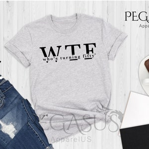 May include: Gray heather athletic t-shirt with black text that reads "WTF who's turning fifty".
