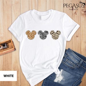 May include: White t-shirt with three Mickey Mouse heads in a row. Each head is a different animal print: giraffe, zebra, and leopard.