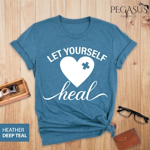 May include: A teal blue t-shirt with the text "Let Yourself Heal" in white. A white heart with a white plus sign is in the center of the text.