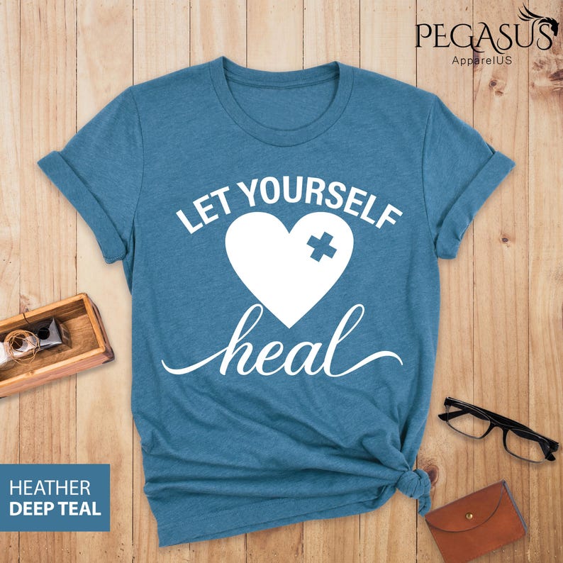 May include: A teal blue t-shirt with the text "Let Yourself Heal" in white. A white heart with a white plus sign is in the center of the text.