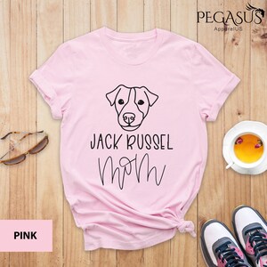 May include: Pink t-shirt with a black graphic of a Jack Russell Terrier dog face and the words "Jack Russel Mom". The shirt is from Pegasus Apparel US.
