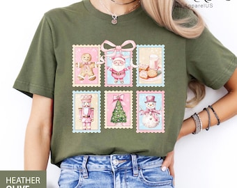 Könnte beinhalten: Heather olivgrünes T-Shirt mit einem farbenfrohen Weihnachtsmarken-Design. Die Marken zeigen einen Lebkuchenmann, den Weihnachtsmann, Kekse und Milch, einen Nussknacker, einen Weihnachtsbaum und einen Schneemann. Das Shirt hat den Text "HEATHER OLIVE".