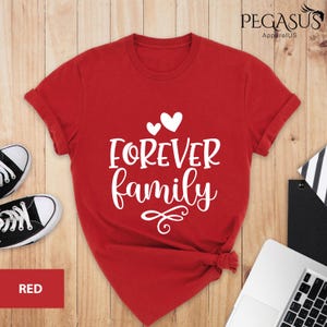 Pode incluir: Camiseta vermelha com texto branco que diz "FOREVER family" com dois cora&ccedil;&otilde;es pequenos e um cora&ccedil;&atilde;o maior acima do texto.