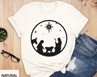 Op de afbeelding: Wit T-shirt met een zwart silhouet van de kerststal in een cirkel. De scène toont Maria, Jozef, baby Jezus, een ezel en een ster.