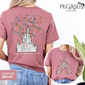 Op de afbeelding: Een heide-paarse t-shirt met een afbeelding van Assepoester's kasteel en Mickey Mouse ballonnen. De tekst "Happiest place on earth" is onder het kasteel gedrukt.
