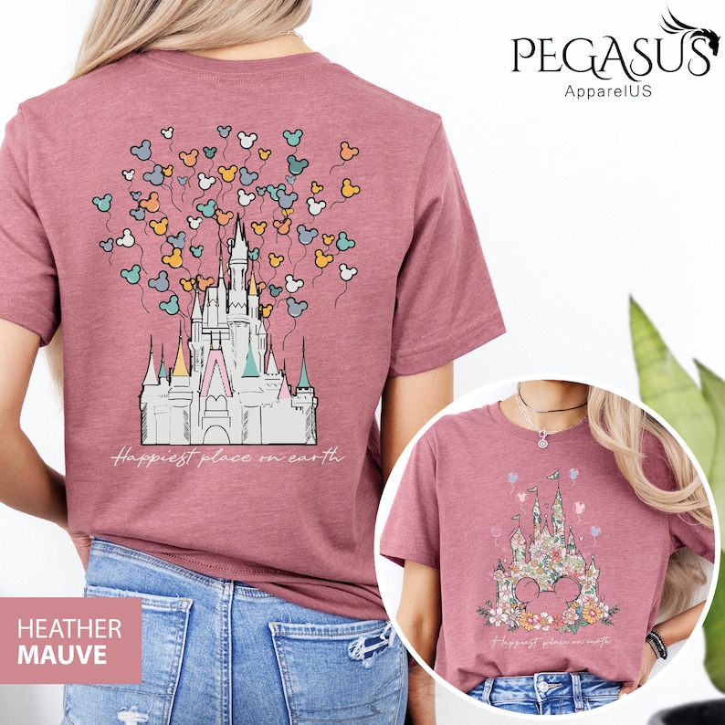 Op de afbeelding: Een heide-paarse t-shirt met een afbeelding van Assepoester's kasteel en Mickey Mouse ballonnen. De tekst "Happiest place on earth" is onder het kasteel gedrukt.