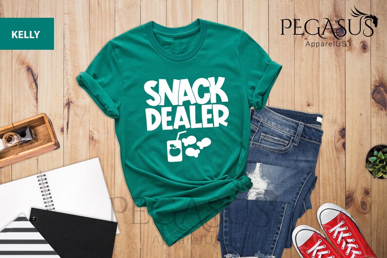 Peut inclure: Un t-shirt vert avec le texte "Snack Dealer" en blanc. Le t-shirt a un graphique d'une boisson et de poissons.