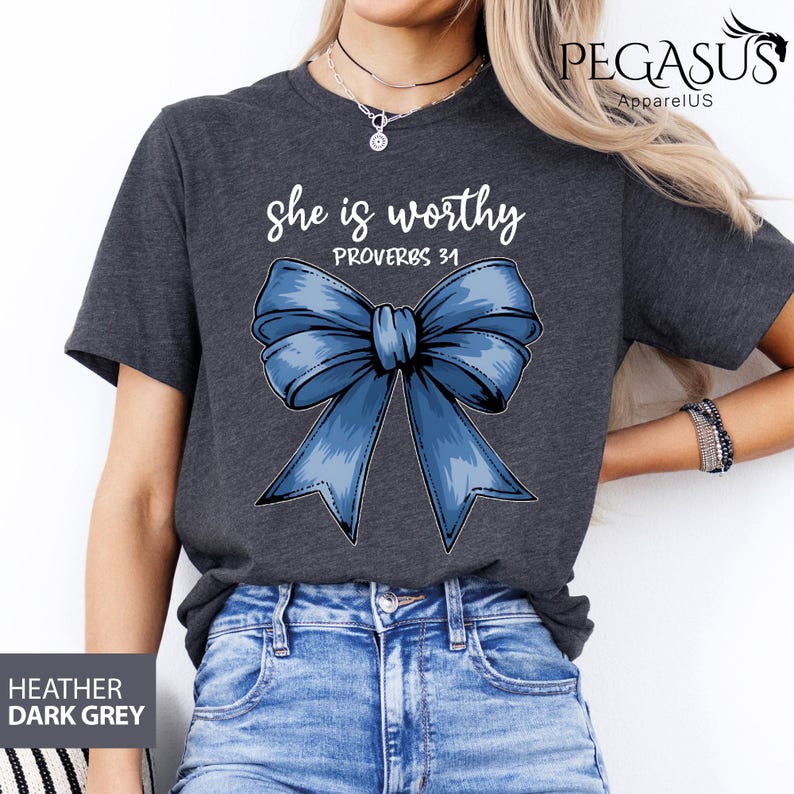 May include: A dark heather grey t-shirt with a blue bow and the text "She is worthy Proverbs 31" printed on the front.