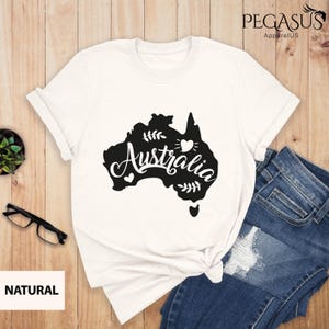 Op de afbeelding: Wit T-shirt met een zwarte omtrek van het continent Australi&euml; en het woord "Australi&euml;" in een gestileerd lettertype. Er zijn kleine hartjes en bloemmotieven rond de omtrek.