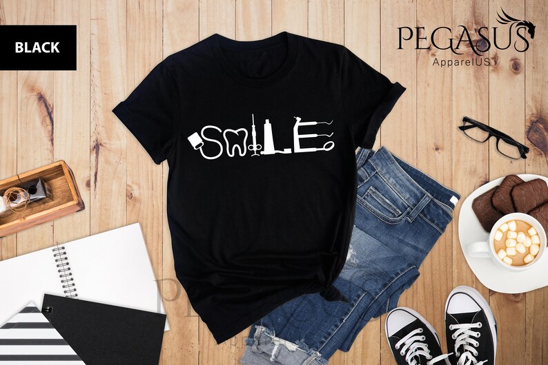 May include: Black t-shirt with a white graphic of dental tools spelling out the word "SMILE".