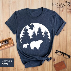Puede incluir: Una camiseta azul marino con una silueta blanca de un oso, un cachorro y un p&aacute;jaro volando sobre una luna con &aacute;rboles en el fondo.