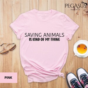 May include: Pink t-shirt with the text "Saving Animals is Kind of My Thing" printed on the front.