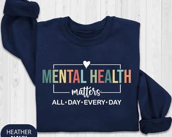May include: A navy blue sweatshirt with the words "MENTAL HEALTH matters" in a rectangular frame, with a white heart above the text. Below the text is "ALL•DAY•EVERY•DAY". The sweatshirt has the words "HEATHER NAVY" in a navy blue circle.