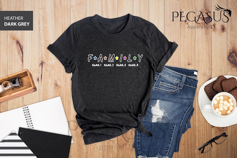 May include: Dark heather grey t-shirt with the word "FAMILY" in white letters with colorful stars between each letter. The text "NAME 1 NAME 2 NAME 3 NAME 4" is printed below the word "FAMILY".