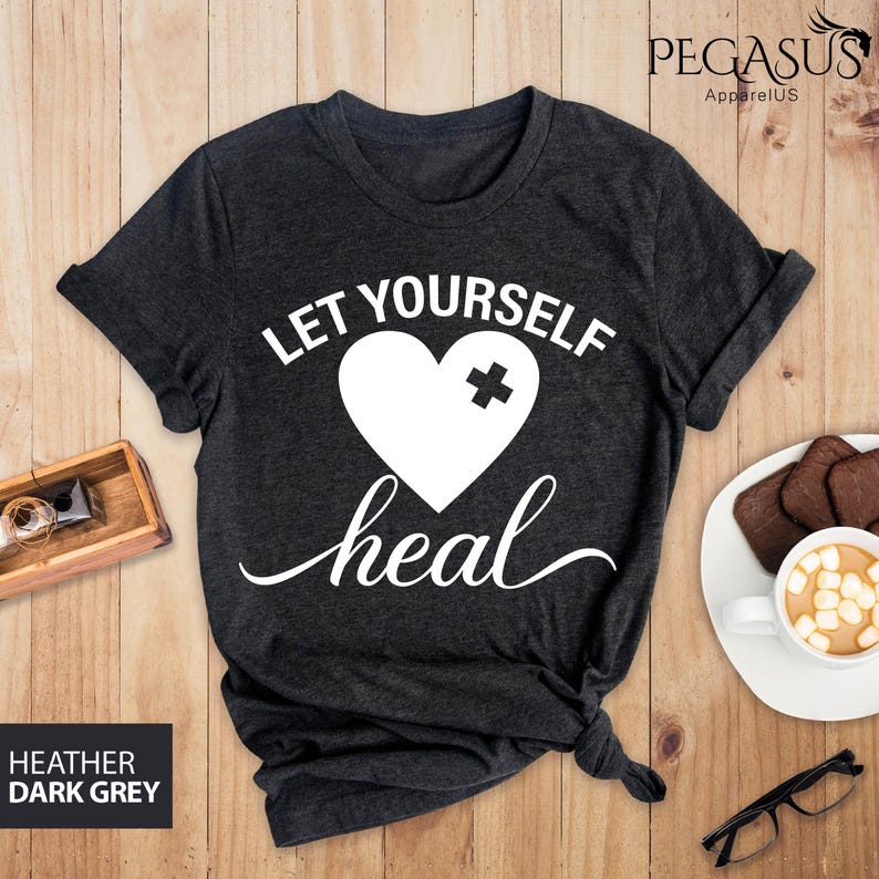 May include: Dark heather grey t-shirt with a white heart with a bandage on it and the text "Let Yourself Heal".