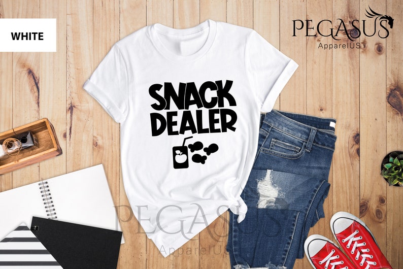 Peut inclure: T-shirt blanc avec un texte noir qui dit "Snack Dealer" et un graphique d'une bo&icirc;te de jus avec une pomme et quelques en-cas.