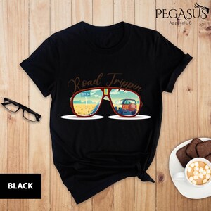 Peut inclure: T-shirt noir avec un graphique de lunettes de soleil refl&eacute;tant une sc&egrave;ne de road trip. Le texte "Road Trippin'" est au-dessus des lunettes de soleil.