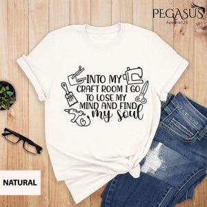 K&ouml;nnte beinhalten: Wei&szlig;es T-Shirt mit schwarzem Text und Grafiken, die "Into my craft room I go to lose my mind and find my soul" lauten. Die Grafiken beinhalten einen Pinsel, eine S&auml;ge, eine Bohrmaschine, eine N&auml;hmaschine und eine Schere.