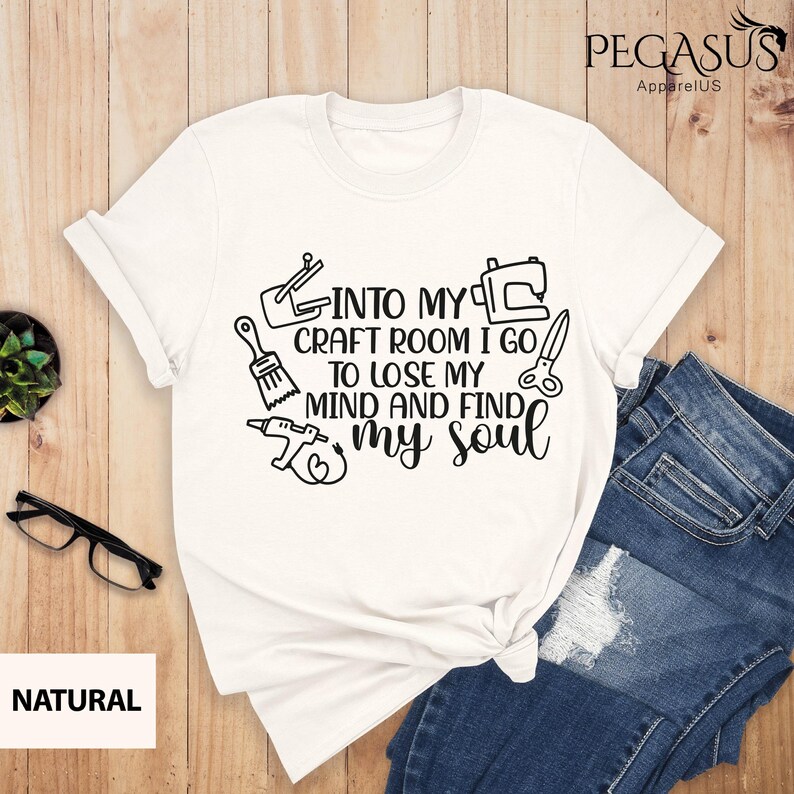 K&ouml;nnte beinhalten: Wei&szlig;es T-Shirt mit schwarzem Text und Grafiken, die "Into my craft room I go to lose my mind and find my soul" lauten. Die Grafiken beinhalten einen Pinsel, eine S&auml;ge, eine Bohrmaschine, eine N&auml;hmaschine und eine Schere.