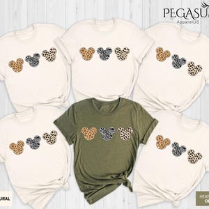 May include: Set of six t-shirts featuring a row of three cartoon Mickey Mouse heads with different animal print patterns. The shirts are in natural and heather olive colors. The text "Pegasus ApparelUS" is in the top right corner of the image.