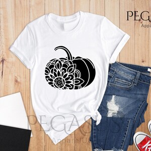 May include: White t-shirt featuring a black and white graphic of a pumpkin with a floral design. The text "PEGASUS ApparelUS" is visible in the top right corner of the image.