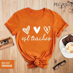 May include: Orange t-shirt with white text that says "esl teacher" and three white hearts. The hearts are drawn in different styles.