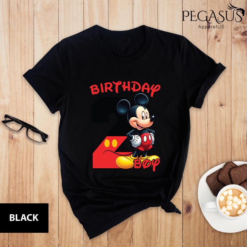 May include: Black t-shirt featuring a Mickey Mouse graphic with the words "BIRTHDAY BOY" in red and yellow. The number "2" is incorporated into the design. The shirt is from Pegasus ApparelUS.