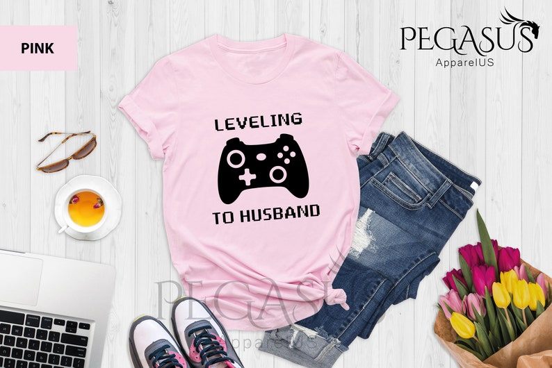 May include: Pink t-shirt with a black video game controller graphic and the text "LEVELING TO HUSBAND".