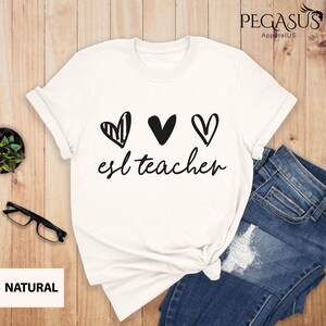 May include: White t-shirt with three black hearts and the text "esl teacher" printed on the front.