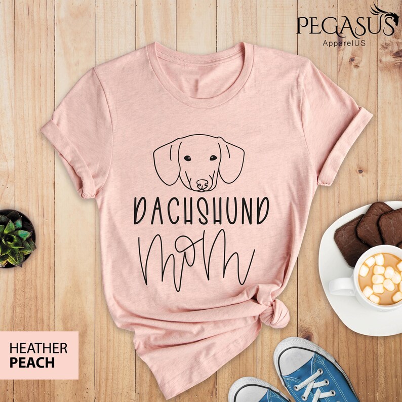 May include: A pink t-shirt with a black outline of a dachshund and the text "Dachshund Mom" in black.