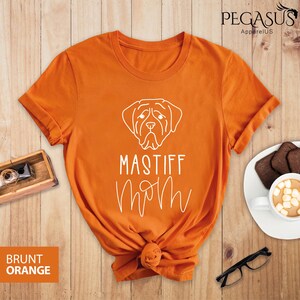 K&ouml;nnte beinhalten: Orangefarbenes T-Shirt mit einer wei&szlig;en Umrandung eines Mastiff-Hundekopfes und dem Text "Mastiff Mom" in einer kursivschrift.