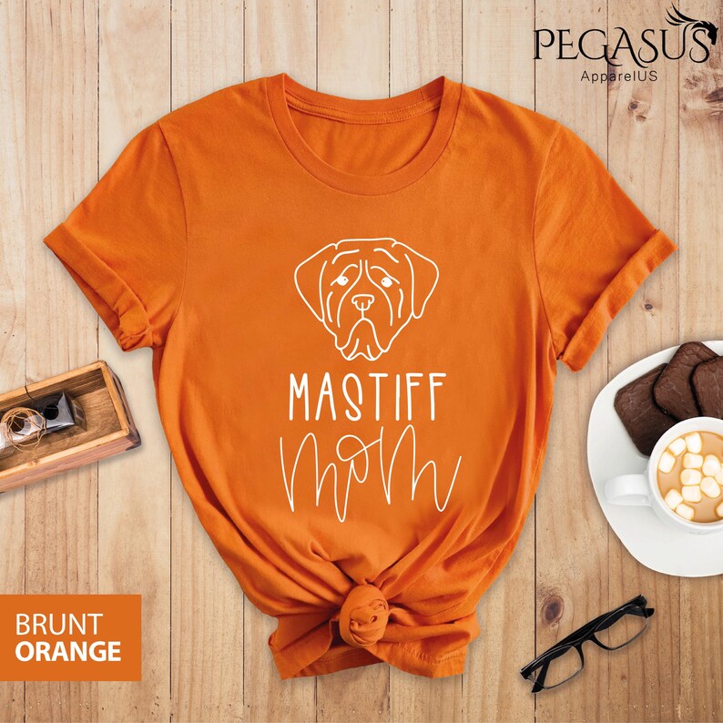 K&ouml;nnte beinhalten: Orangefarbenes T-Shirt mit einer wei&szlig;en Umrandung eines Mastiff-Hundekopfes und dem Text "Mastiff Mom" in einer kursivschrift.