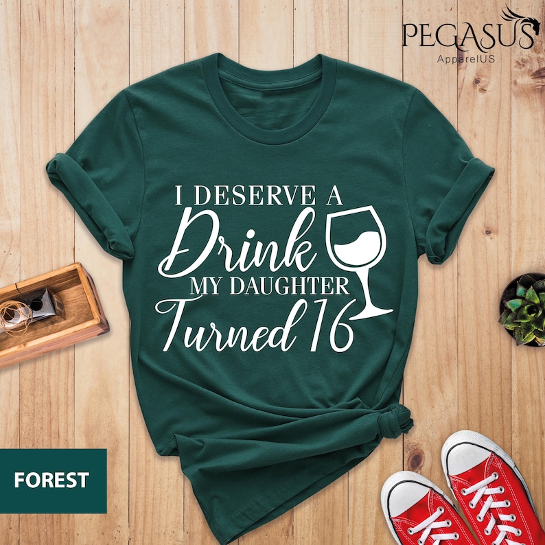May include: A dark green t-shirt with white text that reads "I deserve a drink my daughter turned 16" and a white wine glass graphic.