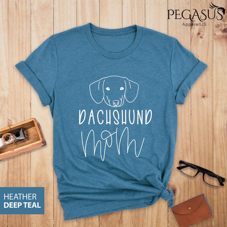 May include: A teal blue t-shirt with a white dachshund outline and the text "Dachshund Mom" in white.