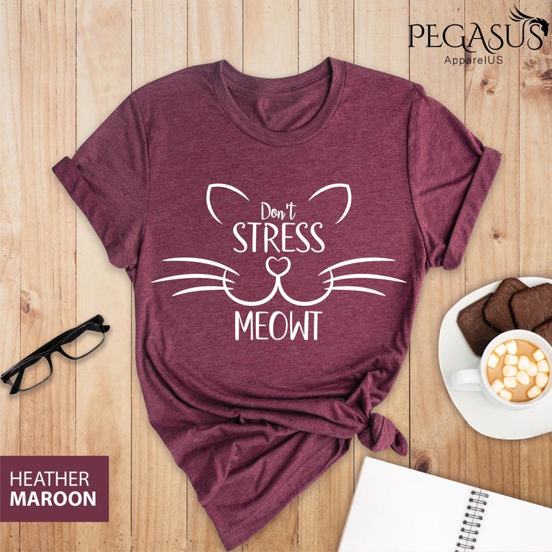 Op de afbeelding: Heather maroon t-shirt met een witte kattenkop-afbeelding en de tekst "Don't Stress Meowt".