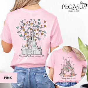 Op de afbeelding: Roze T-shirt met een afbeelding van een kasteel en ballonnen met de tekst "Happiest place on earth".