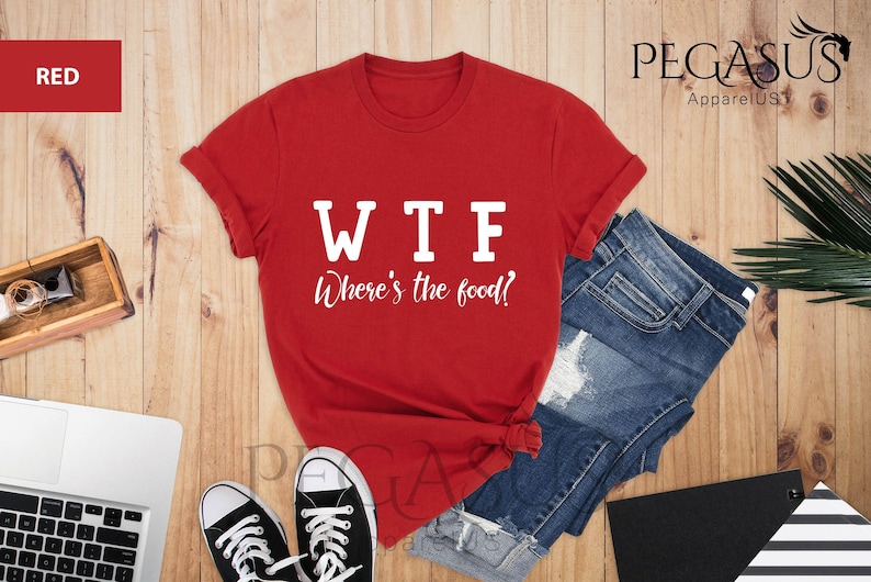 May include: Red t-shirt with white text that reads "WTF Where's the food?" The shirt is laid out on a wooden surface with a pair of black trainers and a pair of blue denim shorts.