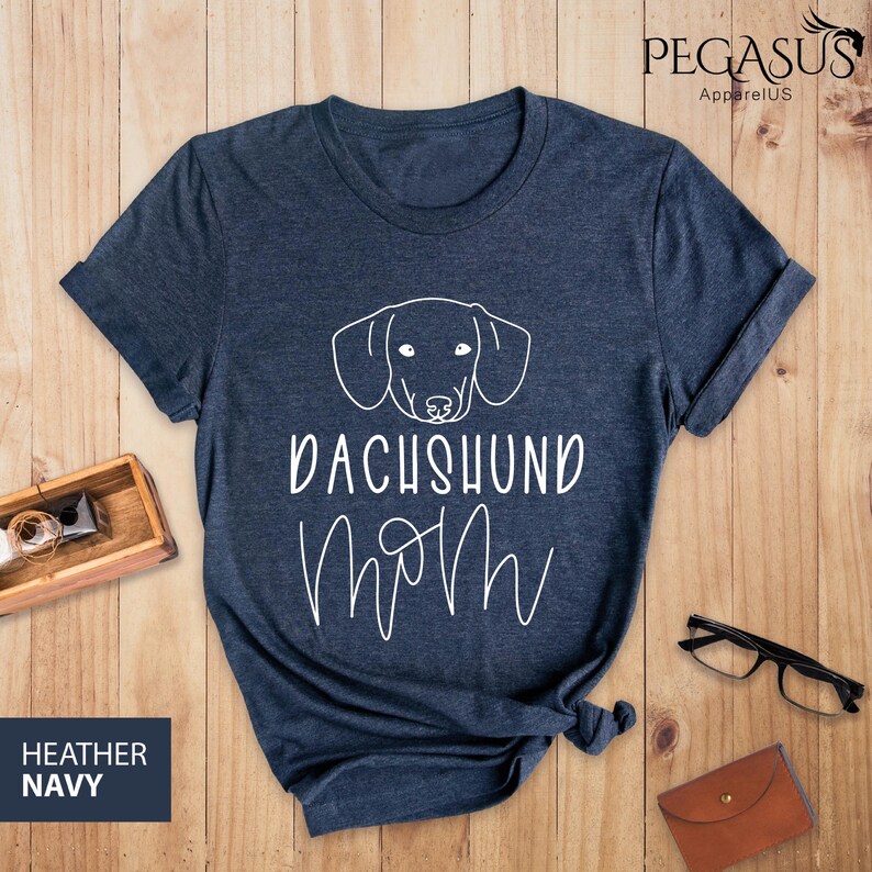 May include: A heather navy blue t-shirt with a white outline of a dachshund and the text "Dachshund Mom" in white.