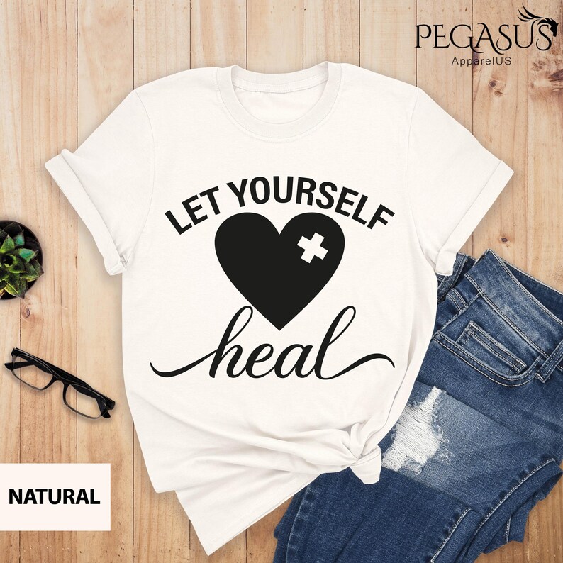 May include: White t-shirt with a black heart with a white plus sign on it and the text "Let Yourself Heal" in black.