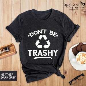 May include: Dark heather grey t-shirt with a white graphic that says "Don't Be Trashy" with a recycling symbol.