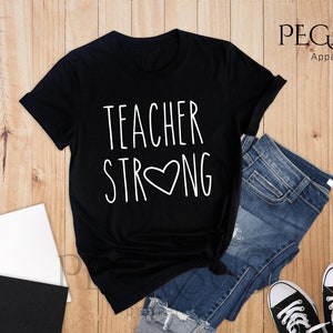 May include: Black t-shirt with white text that reads "Teacher Strong" with a heart in the middle of the word "Strong".