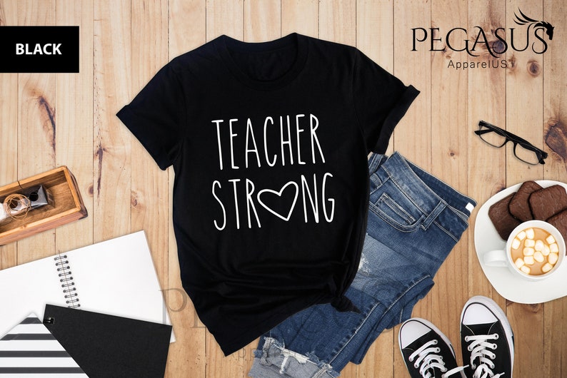 May include: Black t-shirt with white text that reads "Teacher Strong" with a heart in the middle of the word "Strong".