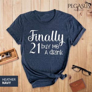 May include: A navy blue t-shirt with the text "Finally 21 buy me a drink" in white.