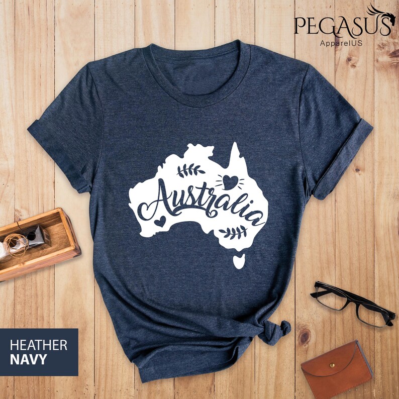 Op de afbeelding: Een heideblauw t-shirt met een witte omtrek van het continent Australi&euml; en het woord "Australia" in een gestileerd lettertype. Een klein wit hartje bevindt zich binnen de omtrek van het continent.